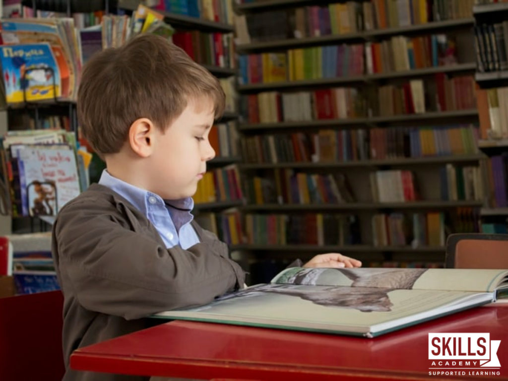 A young boy sitting in a library looking through a picture book. You can help kids interpret images with our Child Psychology Courses.