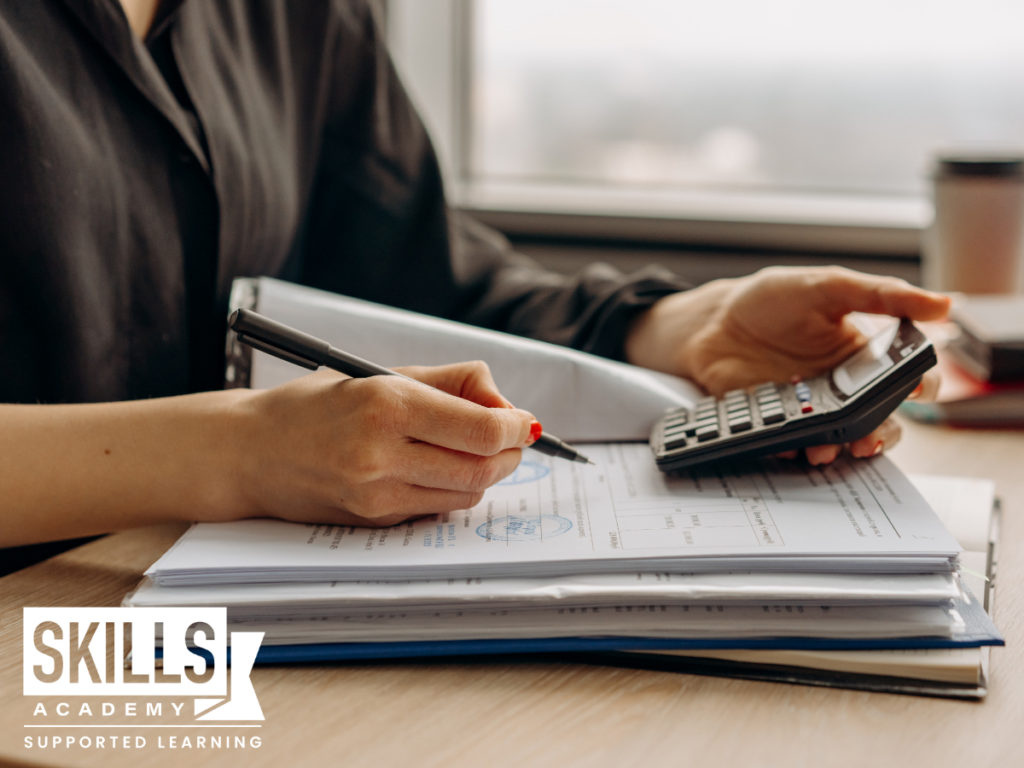 Female financial manager writing in a ledger using a calculator. Learn how to crunch numbers with our Financial Management Courses