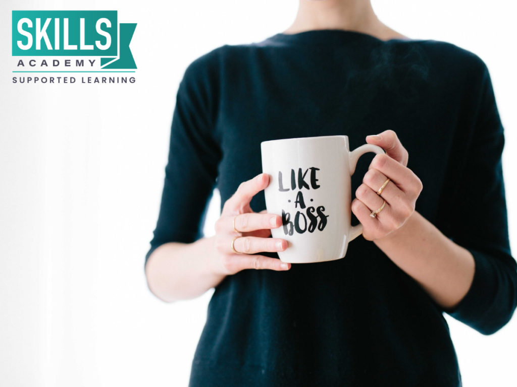 Woman holding a mug standing in front of a white wall gained management skills with our Small Business Management Courses.