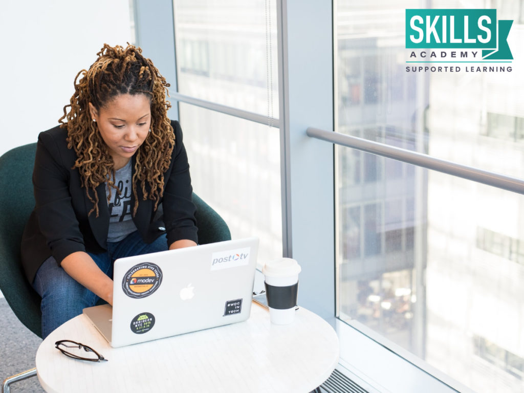 Woman sitting with a laptop by a large window uses the skills she learnt to address feedback given by customers through our Customer Relations Management Courses.