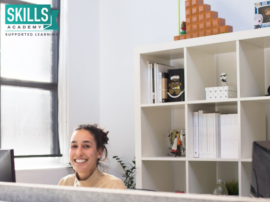A receptionist smiling behind her desk. Get skilled and enrol into our Receptionist Courses