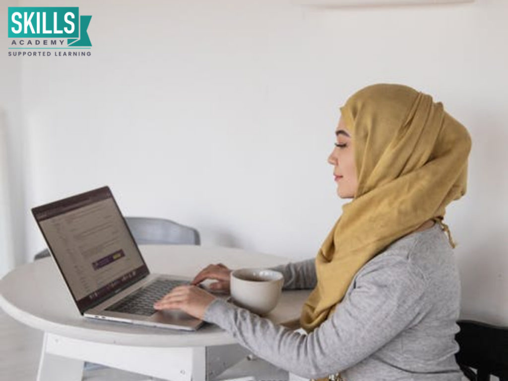 A young woman sitting at her table, wearing a hijab, researching colleges where you can study without matric on her laptop.