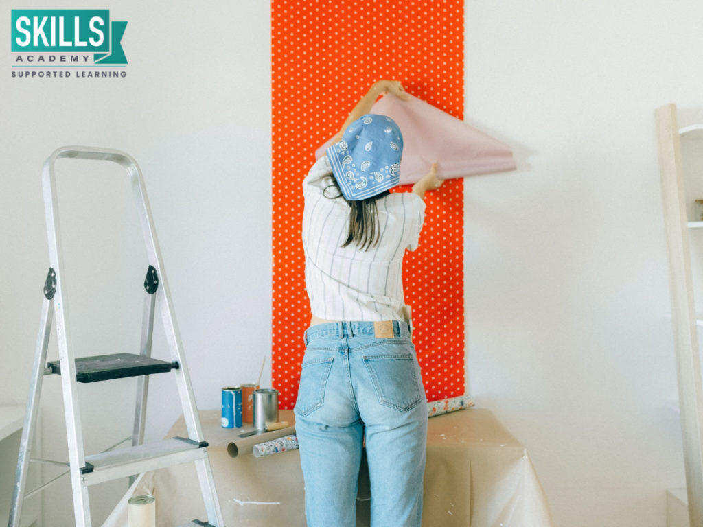 Interior decorator putting wallpaper on a bedroom call. Enhance your creative skills with our Interior Decorating Design and Photography Courses.