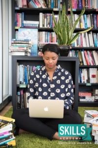 An interior designer seated in front of a book shelf, looking at her laptop