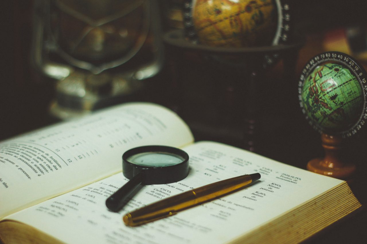 A small magnifying glass and a golden pen on top of a book.