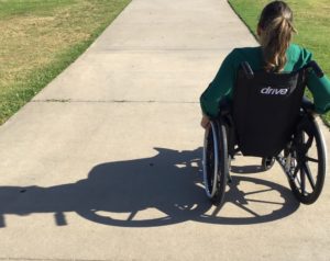 A young woman that has a green top on sitting in her black wheelchair. The back of her wheelchair has the word drive on it. Find out about distance learning benefits for disabled students