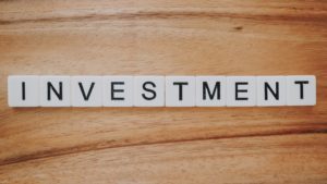 The word "investement" spelts out in letter blocks on top of a wooden table