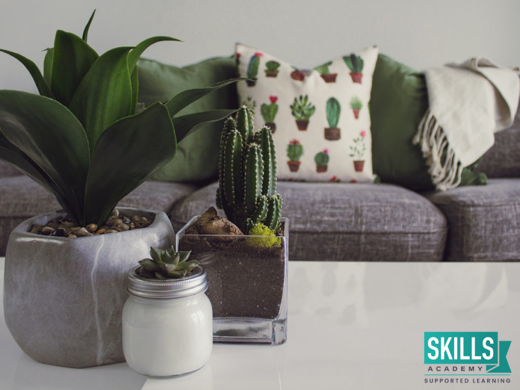A couch and table decorated with green plants and pillows. This can be done using Essential Skills for an Interior Decorator
