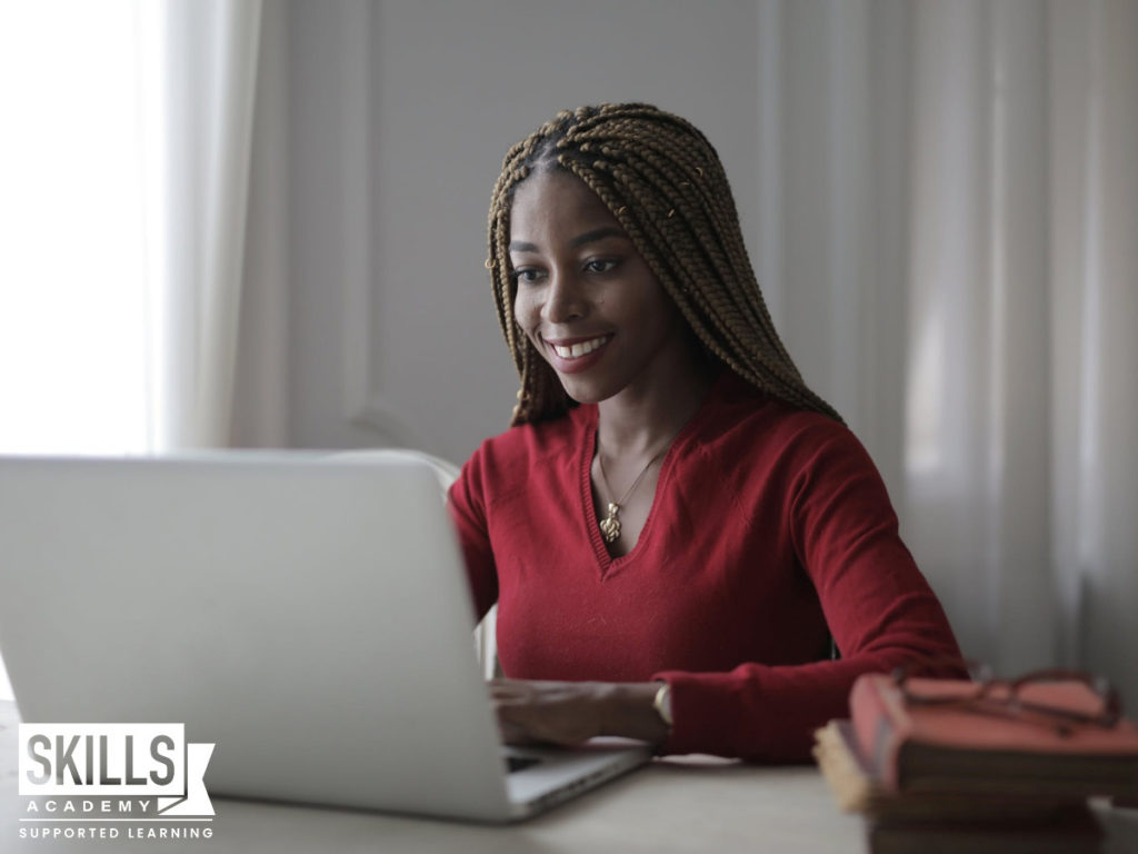 A young student wearing a red top, sitting in front of a laptop, looking at information to help her decide if she should study or work after matric.