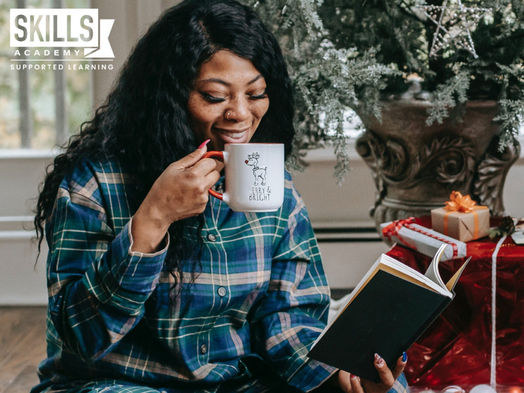 Women studying and drinking coffee while sitting under a Christmas tree. Follow our Money Saving Tips for Students This Festive Season and make this most out of the holiday season.