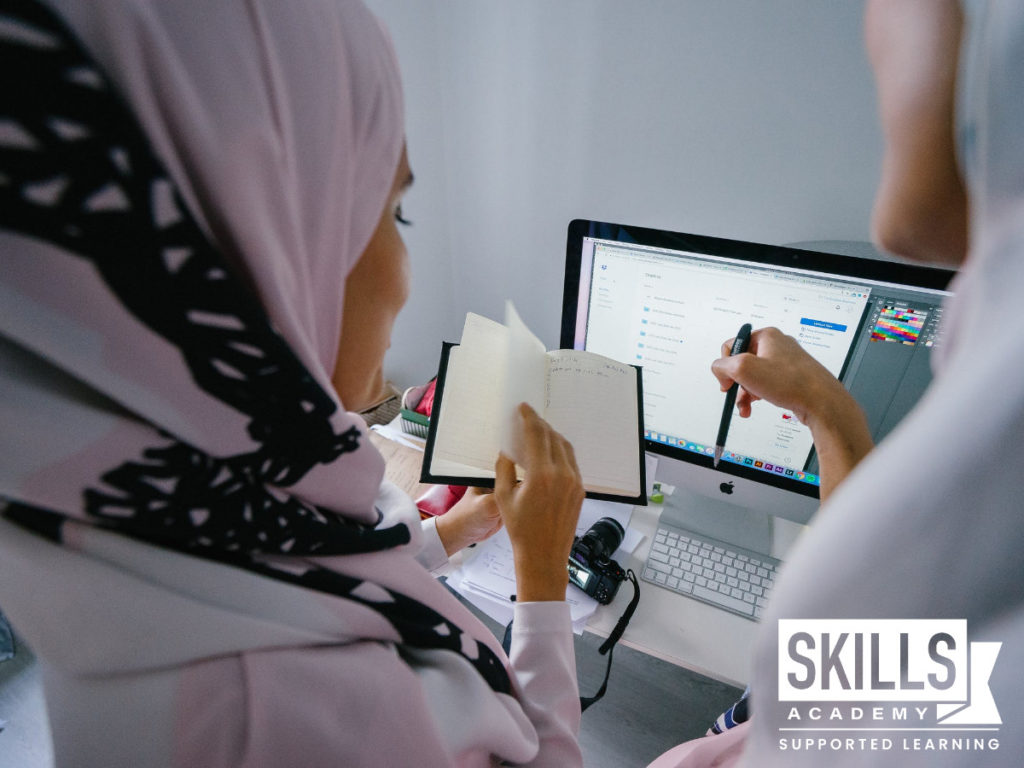 Two ladies wearing hijabs standing in front of a computer making notes on How to Find a job This Festive Season.