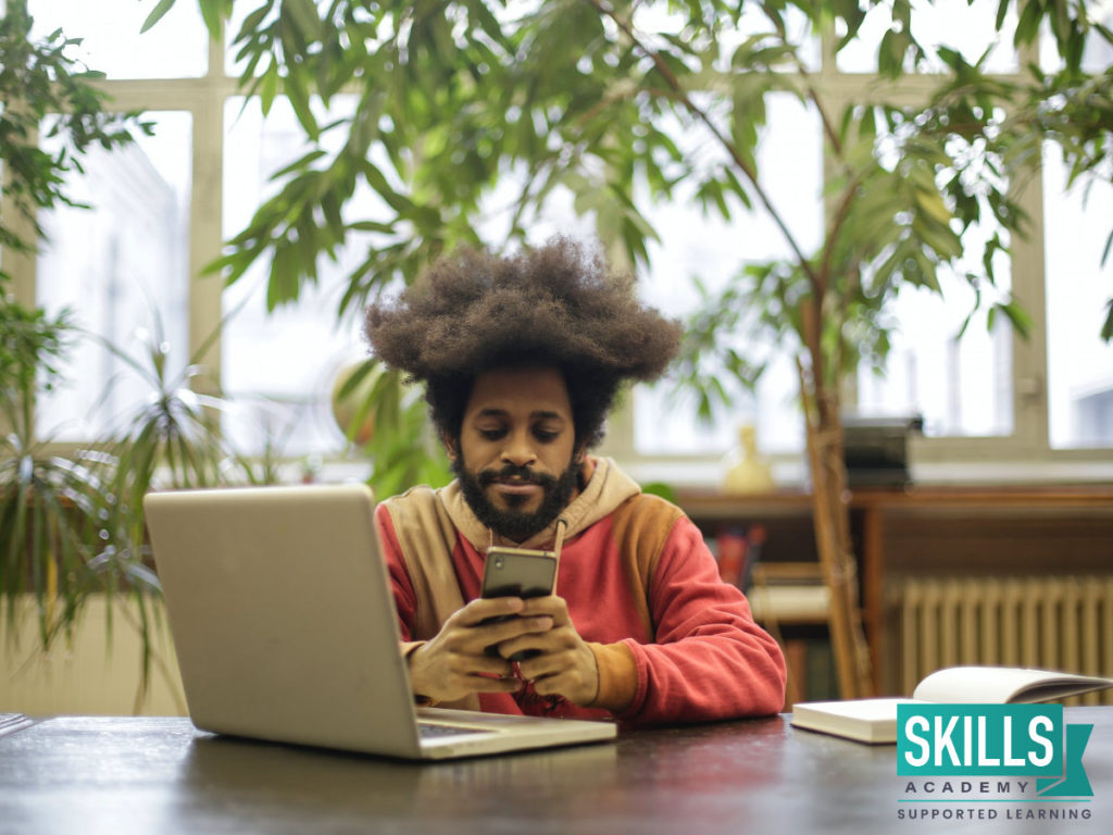 A young man sitting in a library reading up on articles about Managing Stress and Matic Exams.