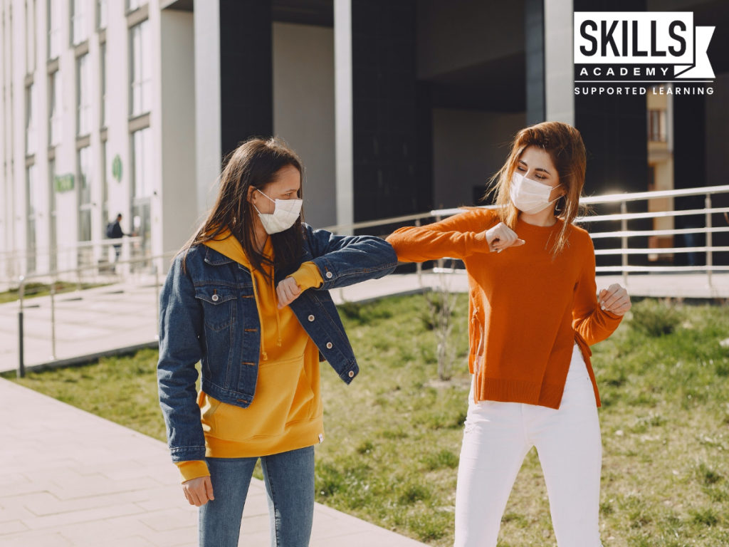 Two matriculants wearing face masks while walking outside of their high school greet each other with their elbow. The Impact of Covid-19 on Matriculants have greatly affected their final year.