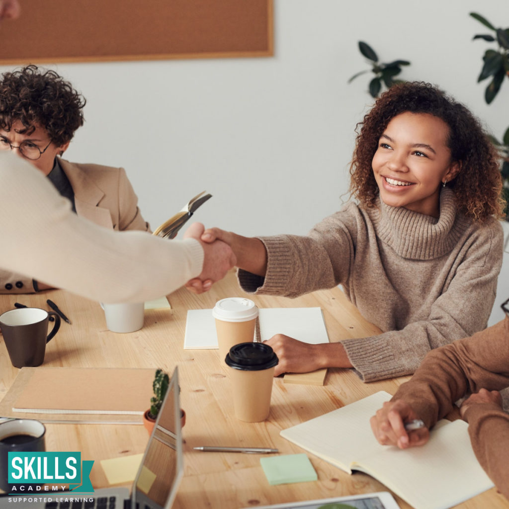 Woman sitting while shaking hands with a man that is standing, congratulating her on getting a job. Learn How to Pass a Personality Test and you could be one step closer to landing your dream job.