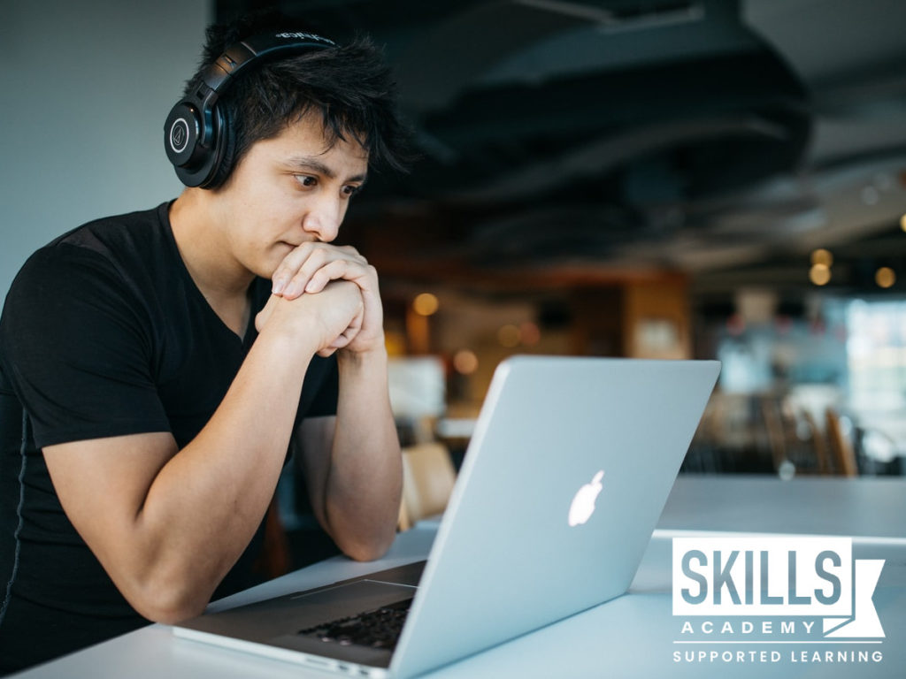 A student sitting with headphones on studying Music Past Papers on his laptop.