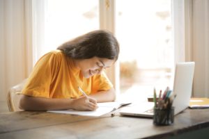 A student wearing a yellow top, sitting at her desk studying for her Nated June Exams 2021.