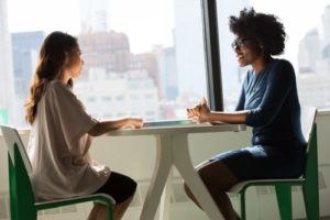 Two business women sitting at a table, having an interview. Getting a job to Jump Start Your Career means acing your interview.