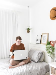 A student sitting on her bed doing freelance work. Find out Why Freelancing is Great to Try During the Holidays.