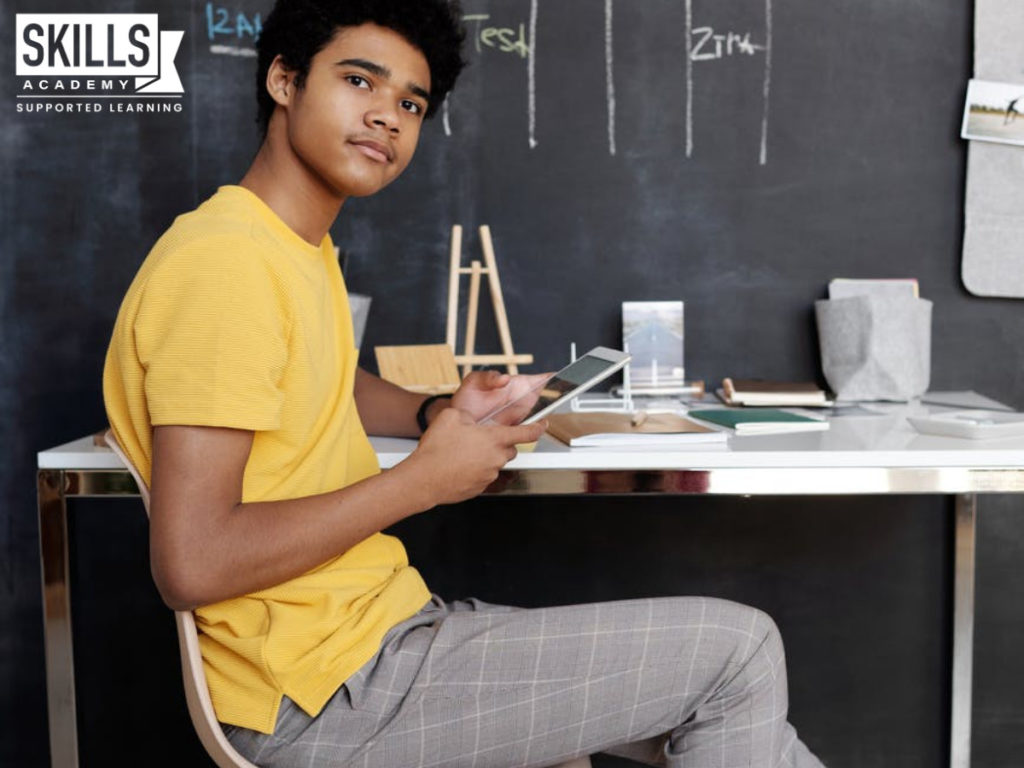 A young boy sitting in front of his study desk with a book in his hand, reading up on Adjusting to Remote Learning.