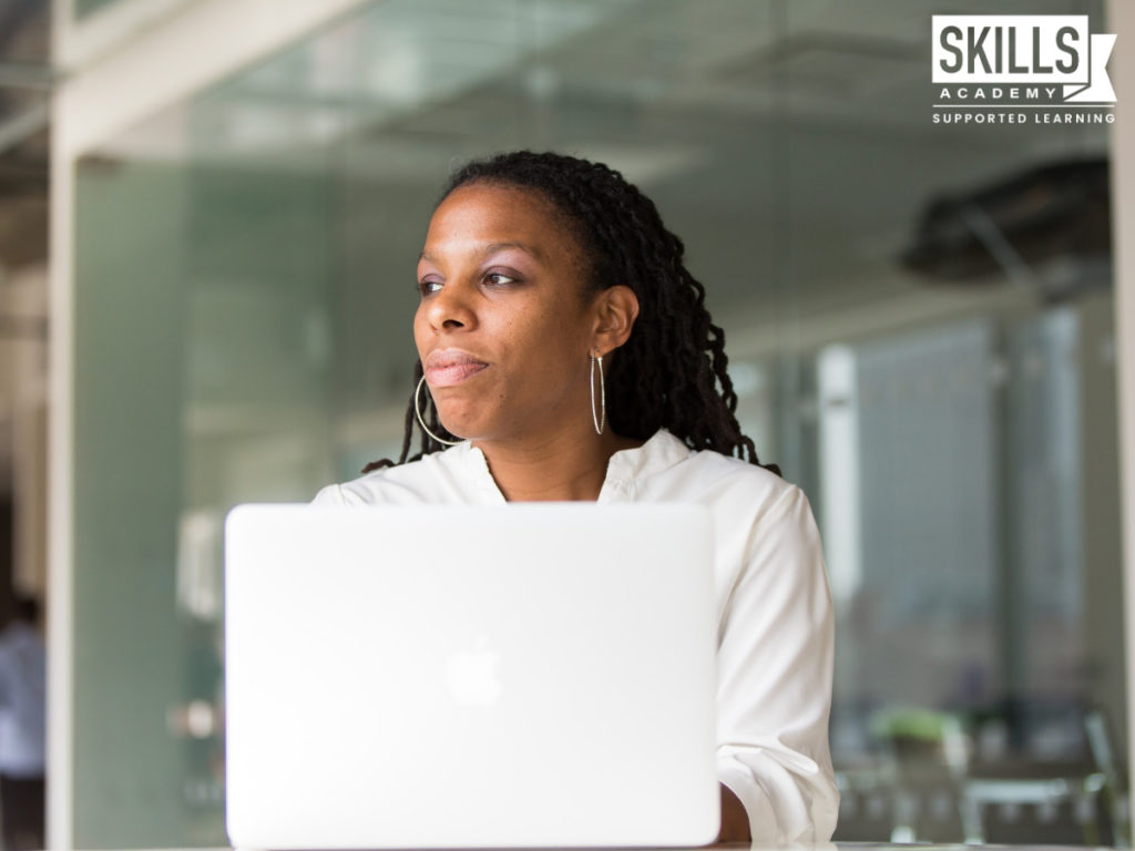 Woman with a laptop in front of her staring out to the side. The benefits of studying an HR Management Course will help you reach your goals.