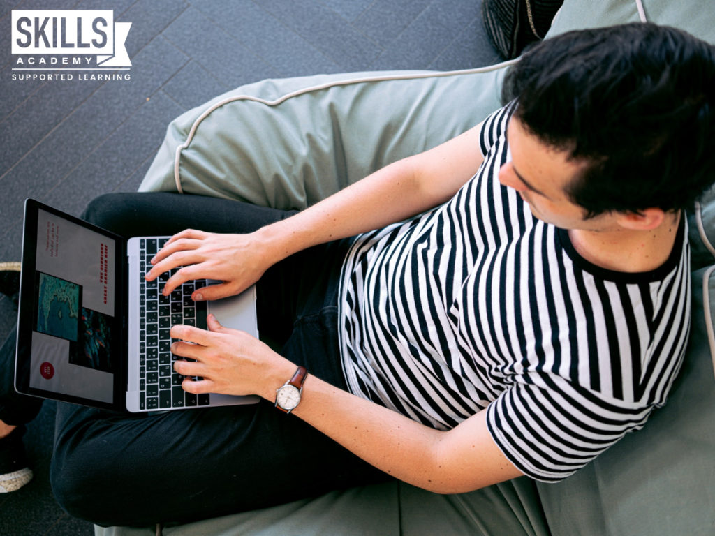 Man wearing a striped t-shirt sits and works on a laptop. Work from the comfort of your home when you gain experience as a freelancer.