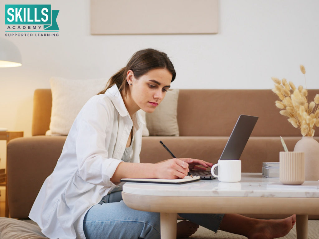 Woman sitting on the floor with a laptop and writing in a book. Learn how remote learning can help your career right here.