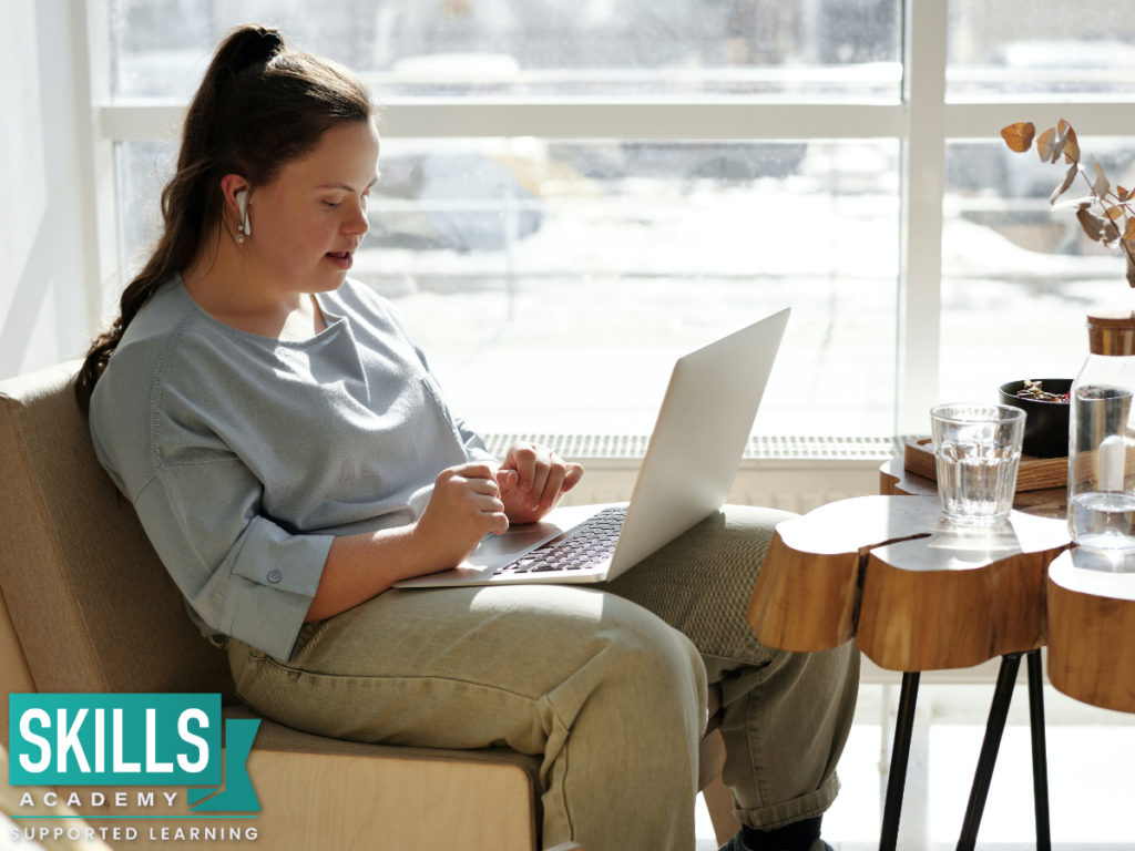 Student sitting with a silver laptop at the window of a cafe and doing her work. More info for ICB Exam Registrations 2021 follows