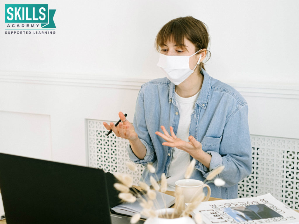 Teacher wearing a cloth face mask is following Safety Protocols While Marking Matric Exam Papers and sitting at a desk maintain social distancing.