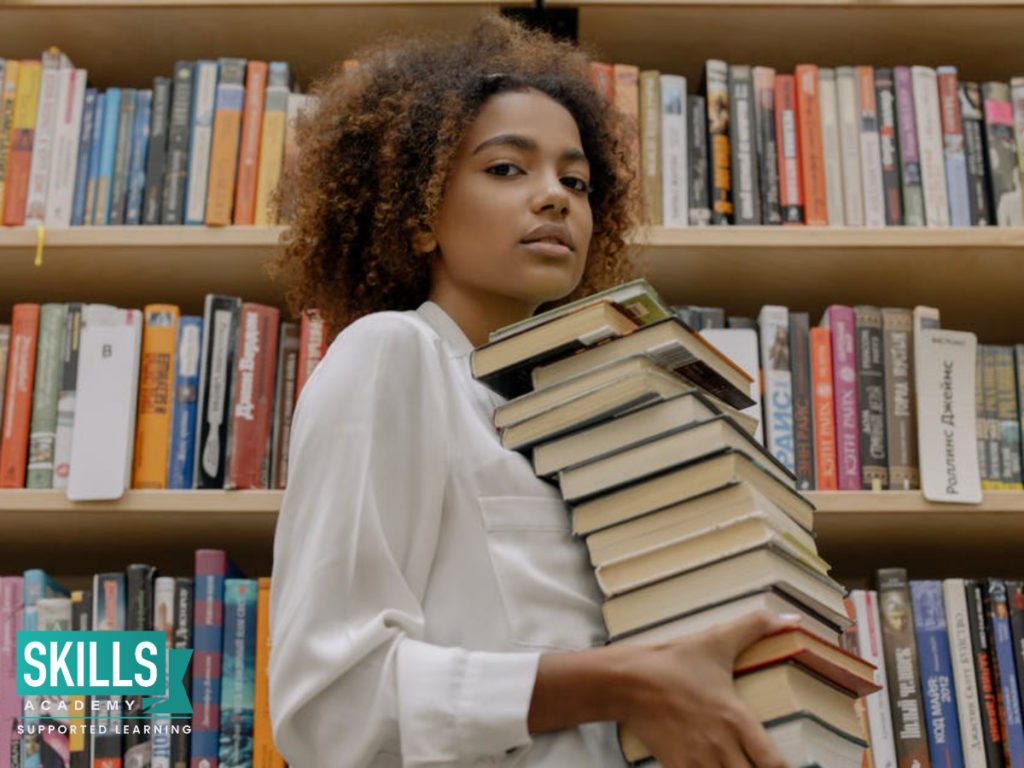 A student holding a stack of books. Follow these 9 habits of successful students to reach academic success.