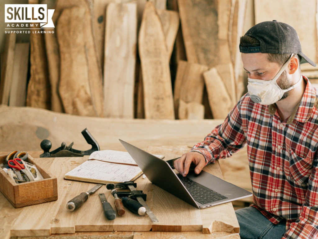 Carpenter wearing a face mask working on a laptop surrounded by wood and tools on a table. Find out what are your chances of getting a job with course specific careers right here.