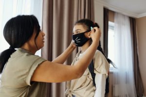 Mother placing a face mask on her daughter. Find tips on How to Prepare for the New School Year right here
