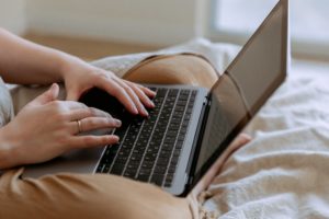 Person in bed typing on a silver laptop. Which NATED Course is Best For me? Find out here