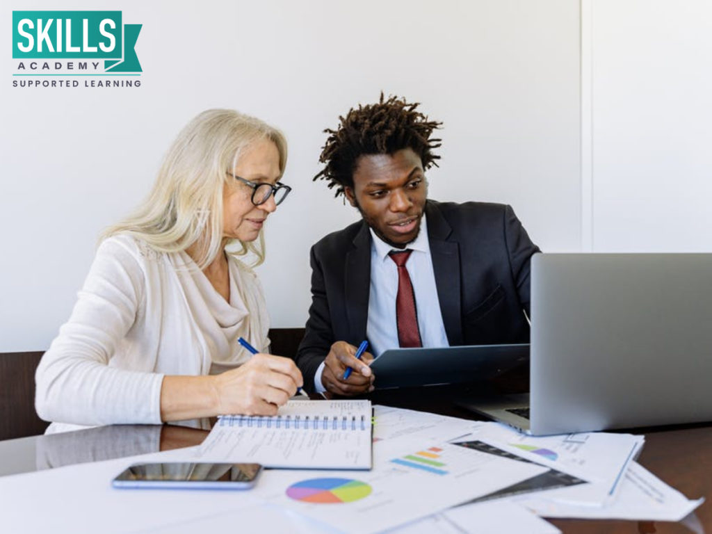 Insurance consultant helping his client set up a retirement plan while sitting at a table looking at a laptop. Finlite in partnership with Skills Academy offers an amazing insurance course.