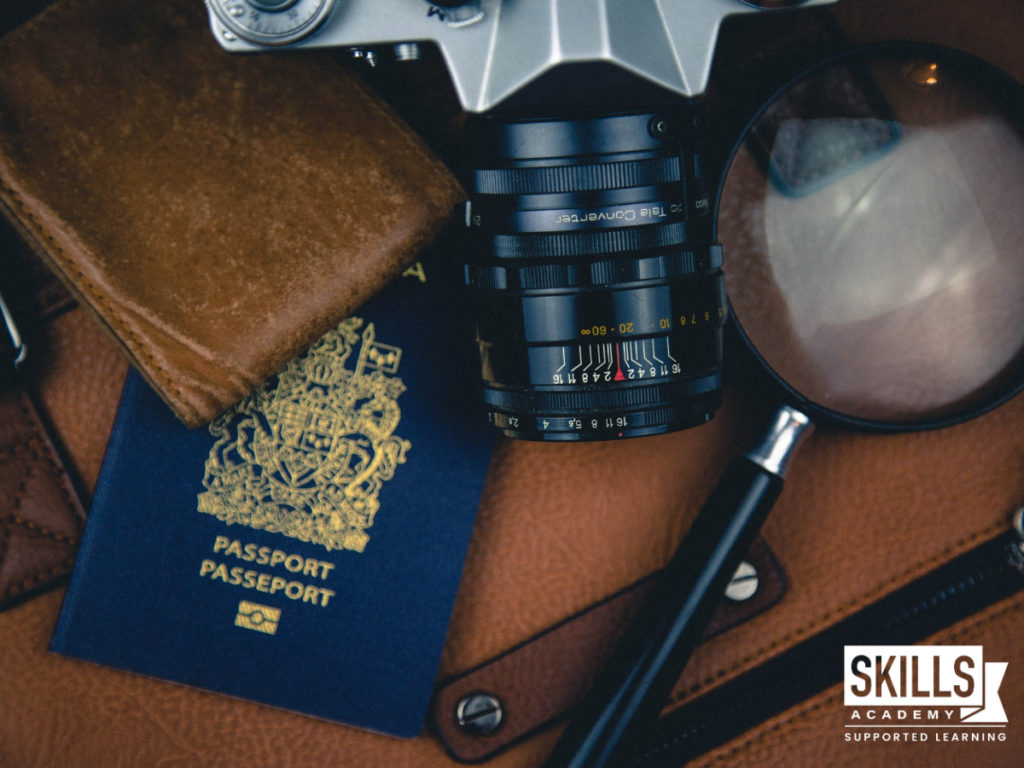 Passport, camera, wallet and magnifying glass laid out on a brown suitcase. Find out what the subjects required to study tourism are right here.