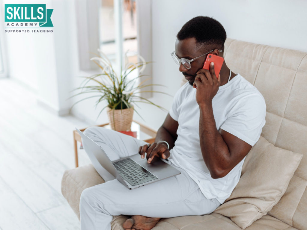 Man sitting on a couch with a laptop resting on his legs while speaking on a cellphone. Upgrade your skills with our accredited courses you can study online with us.
