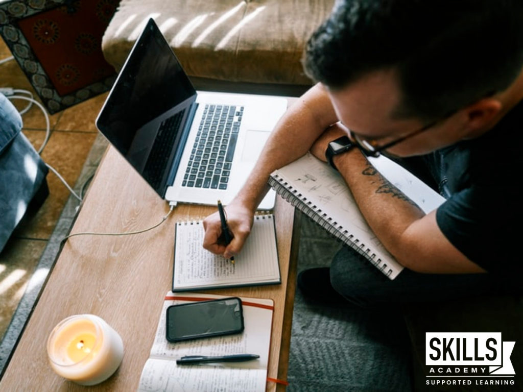 A man writing down the benefits of computer courses he is researching on his computer.