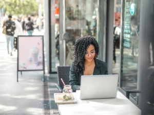 Woman with curly hair sitting at a desk in the city in front pf her pc.
