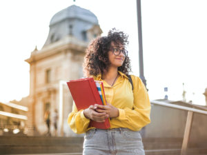 Female student standing with a book in her hand, infornt of her campus.How to Choose the Right Course After my Degree.