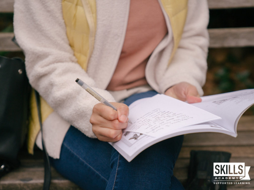 Woman sitting on a bench making notes in a book. Learn how to register to study matric with us right here.