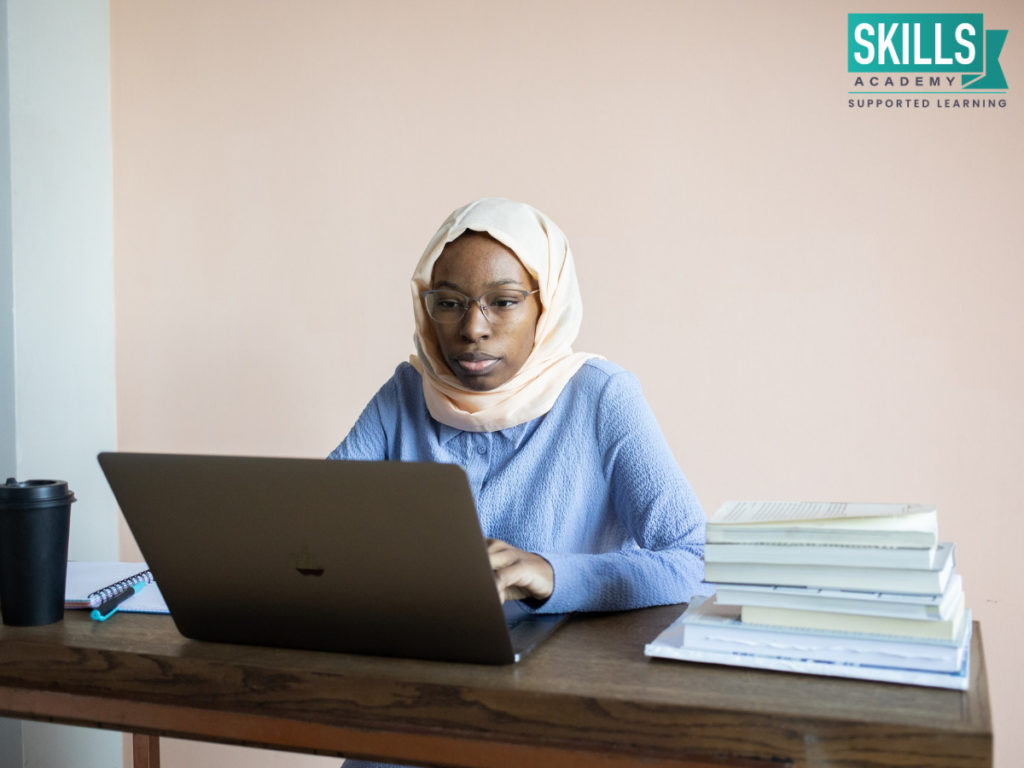 Woman wearing a white scarf and blue top typing on a laptop. Learn where to study matric right here.