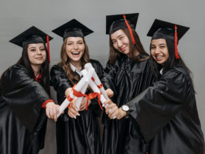 Four female students stading in their graduation gowns. 5 Benefits of Completing a Short Course During Your gap Year.