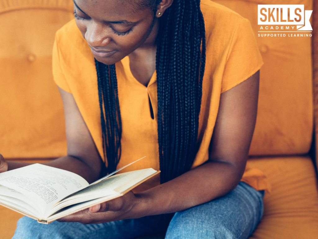 Woman sitting on the couch reading a book, using our tips to improve your reading skills.