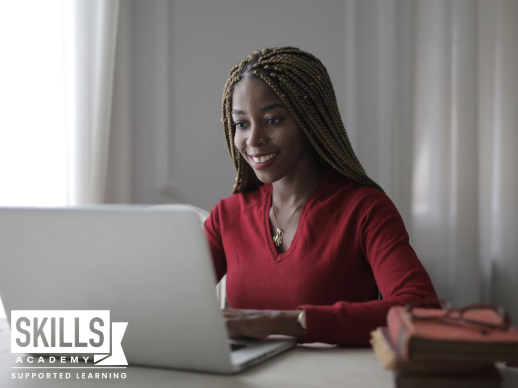 A young girl smiling while she uses her laptop to create her portfolio of evidence. Find out how to create a portfolio of evidence right here.