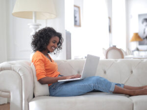 Student sitting on a couch using her laptop to study. Find out about choosing between classroom learning and distance learning here.