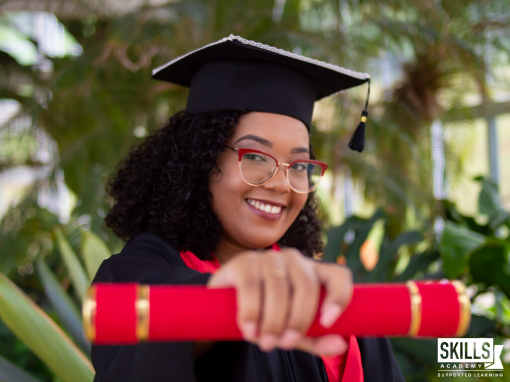 A female student in a graduation cap and gown holding a diploma after knowing the differences between a degree, certificate and diploma. Study our courses today!