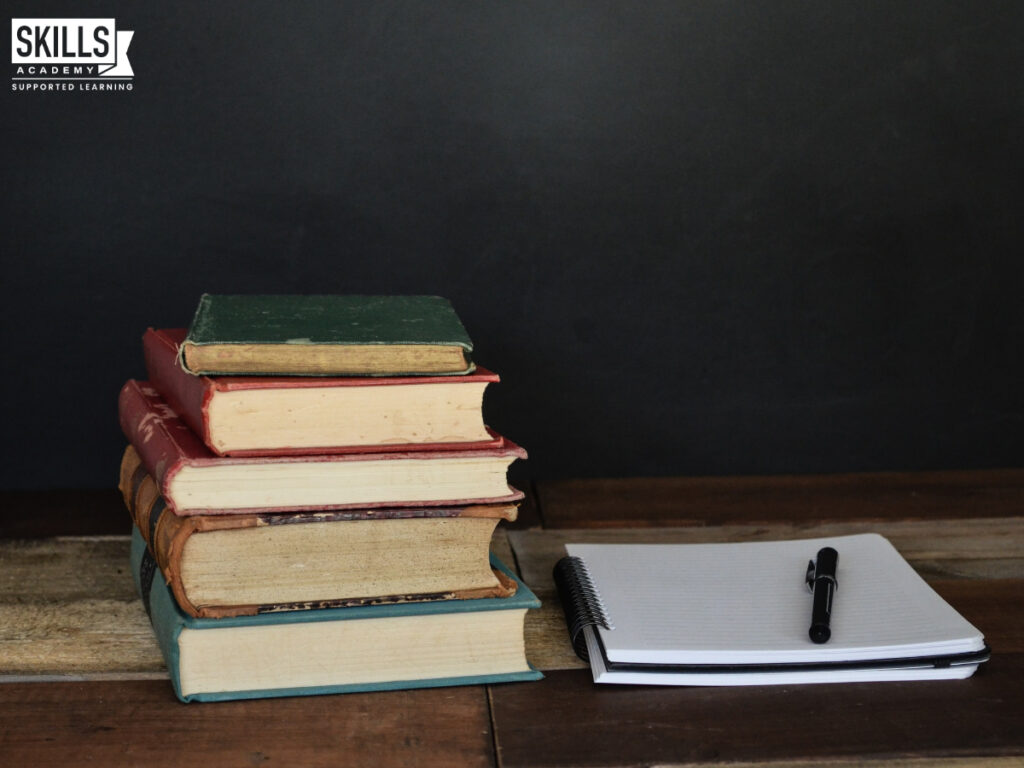 A pile of books next to a writing pad with a pen on top of it. Want to know how to deal with poor matric results? Study our courses today