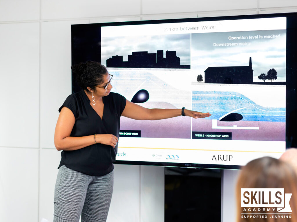 A woman at work pointing to a smart board while giving a presentation and finding ways to deal with presentation nerves. Study with us today.