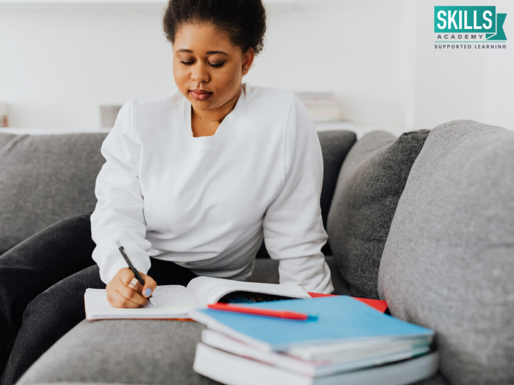Woman sitting on a couch writing in her notebook. Find out how we assist you in your studies.