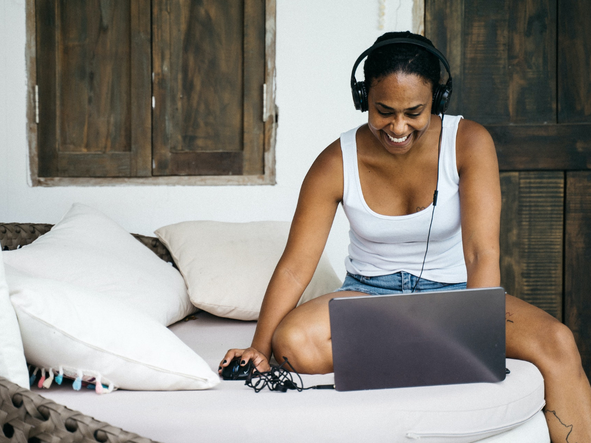 Woman smiling while wearing headphones and typing on a laptop. Take a look at how we assist you in your studies.