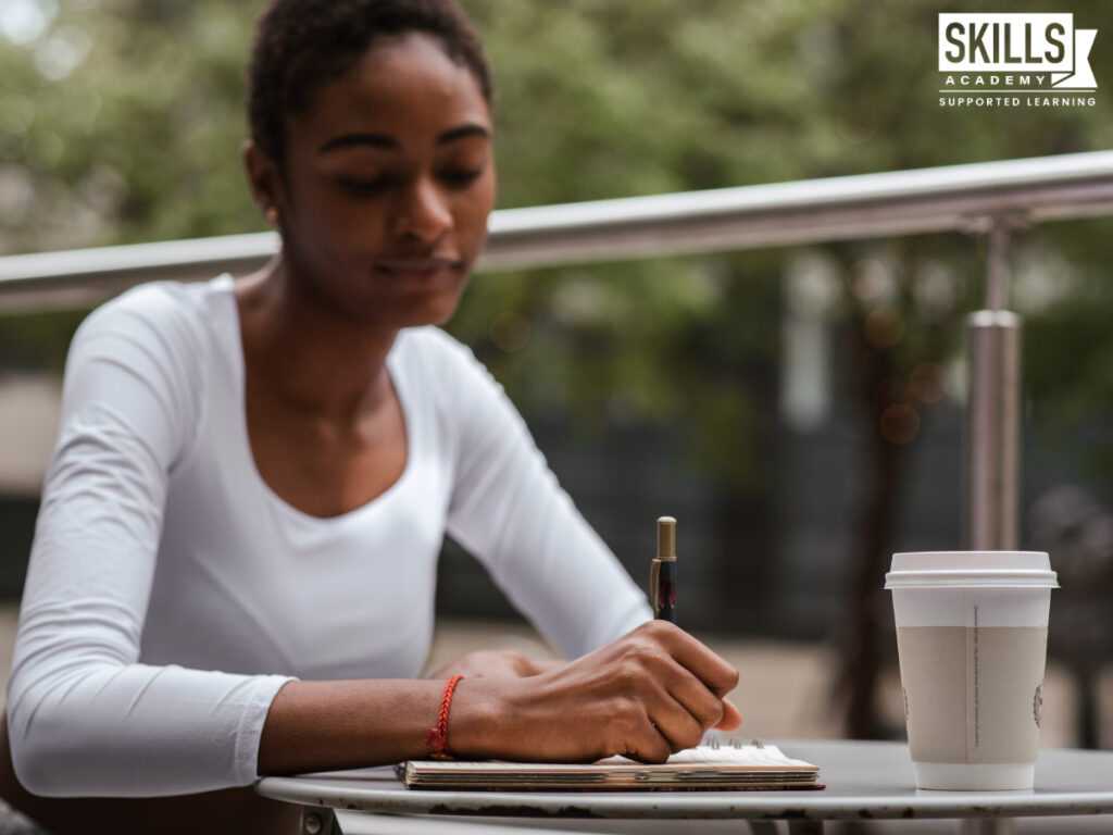 Woman sitting outside at a table while writing in her notebook. Find out what matric subjects we offer here.